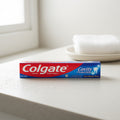 A travel-sized Colgate toothpaste tube on a bathroom counter with a window in the background