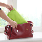 Person placing a green toiletry bag into a red handbag by a window