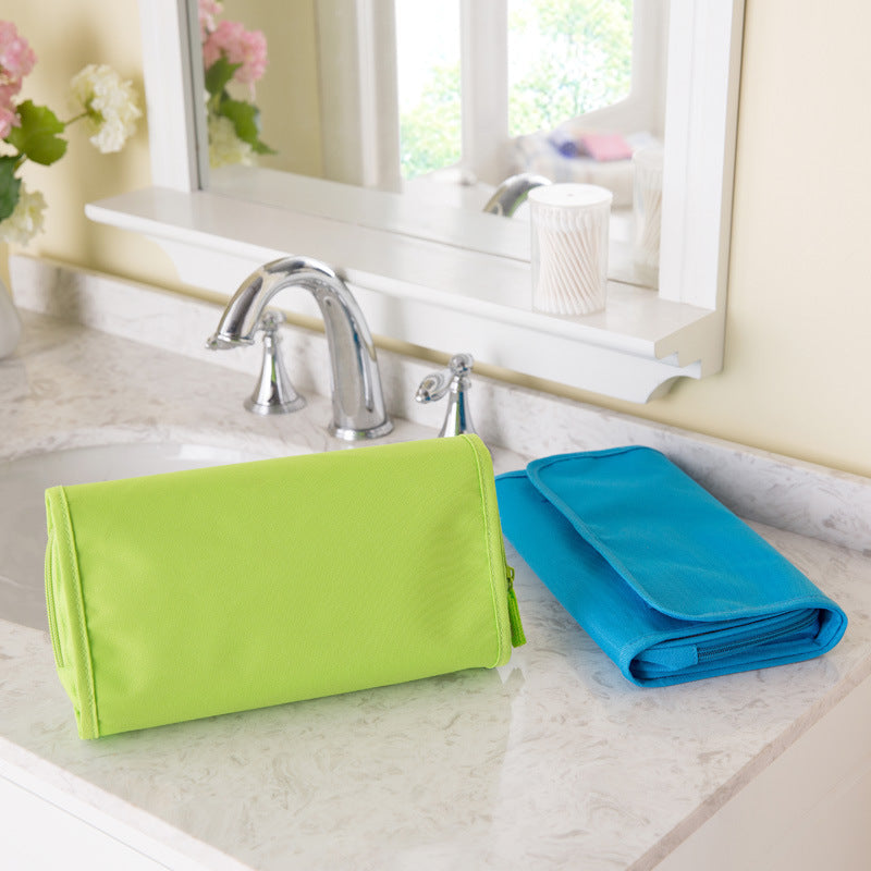 Green and blue folded toiletry bags on a bathroom counter with a mirror and sink in the background.