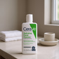 CeraVe hydrating facial cleanser bottle on a bathroom counter with towels and a cup in the background.