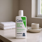 CeraVe hydrating facial cleanser bottle on a bathroom counter with towels and a cup in the background.