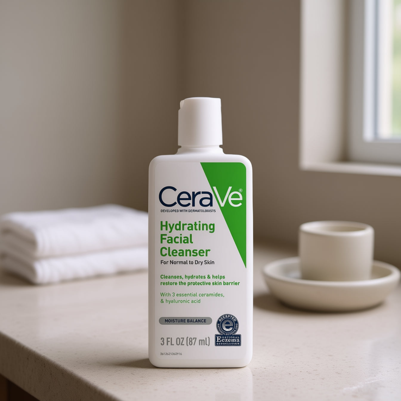 CeraVe hydrating facial cleanser bottle on a bathroom counter with towels and a cup in the background.