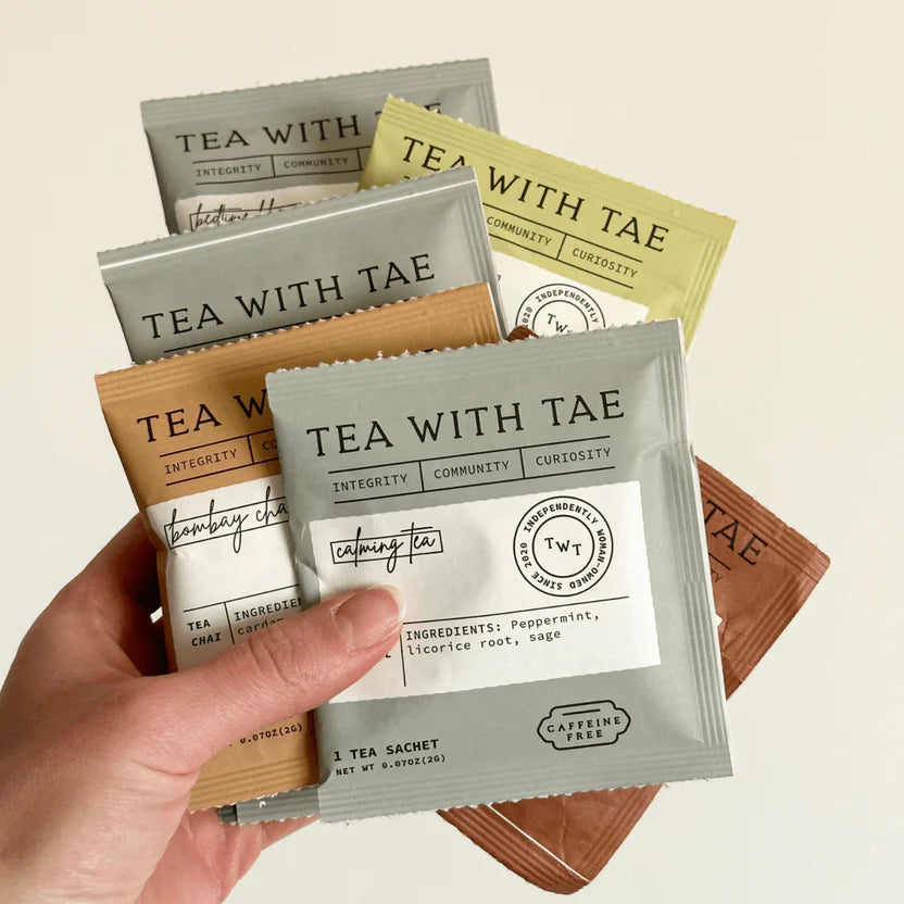 Hand holding a 'Tea with Tae' tea sachet with more sachets in the background.