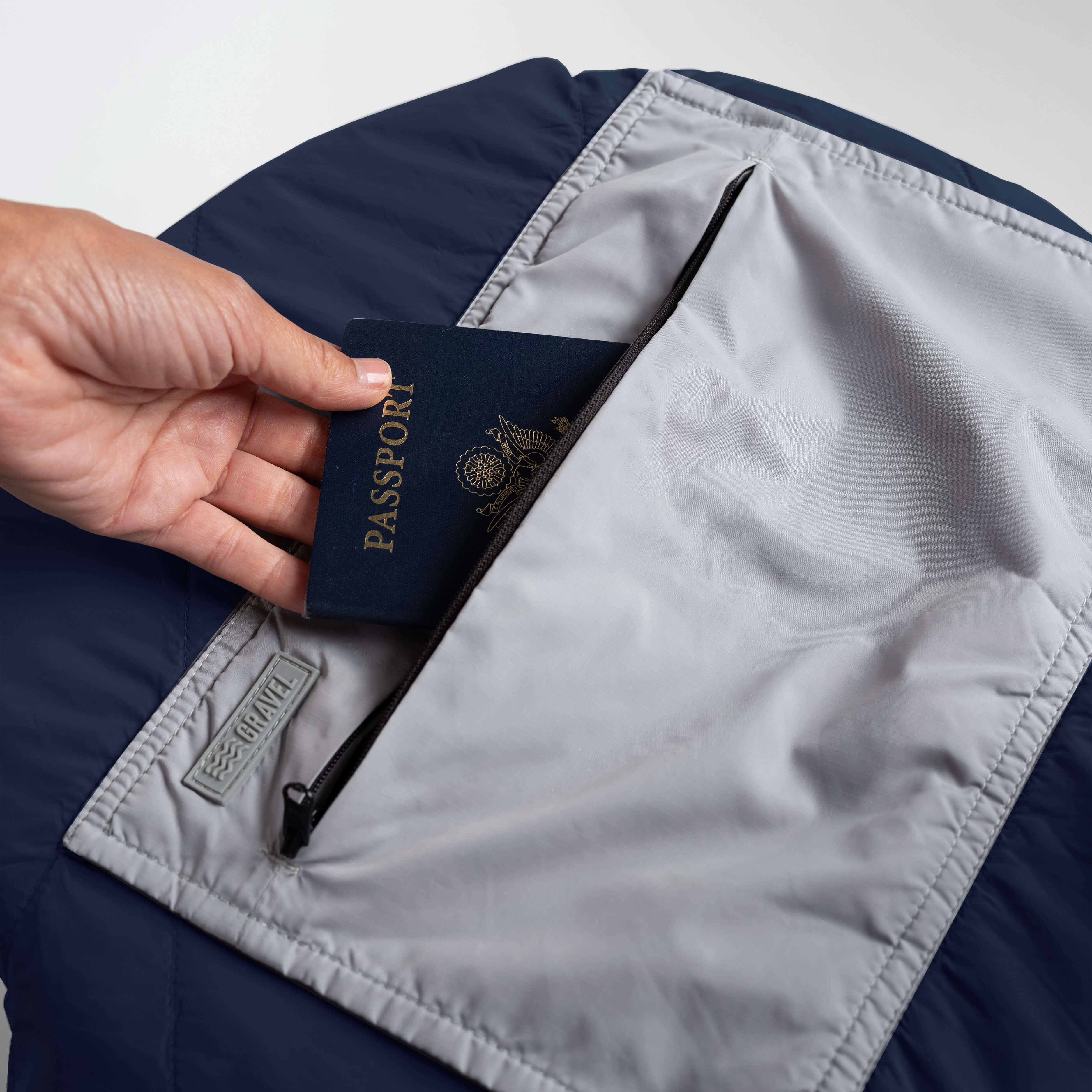 Hand holding a passport inside a navy jacket with a gray lining.