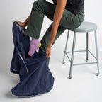 Person sitting on a stool with one foot in a navy blue bag, wearing green pants and pink socks.