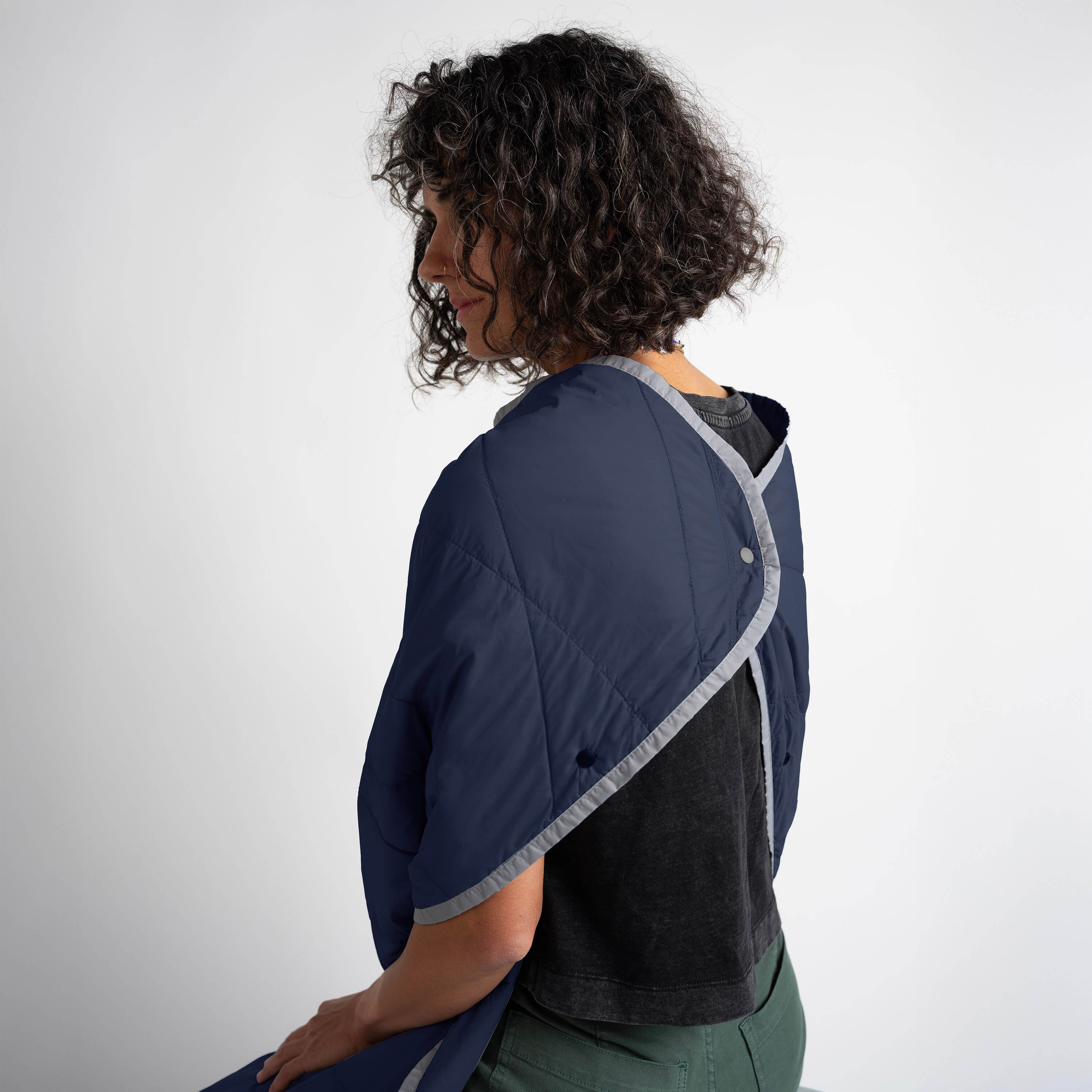 Person wearing a navy blue blanket with gray trim on a white background