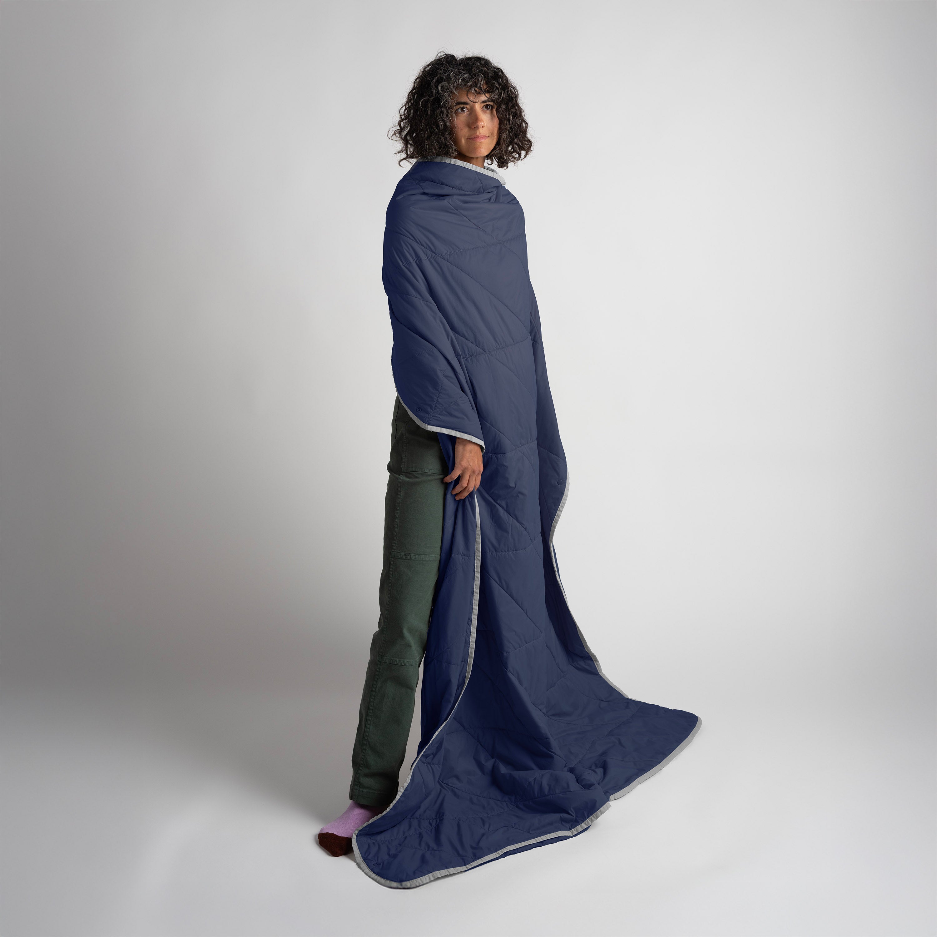 Person wearing a long navy blue blanket on a plain background