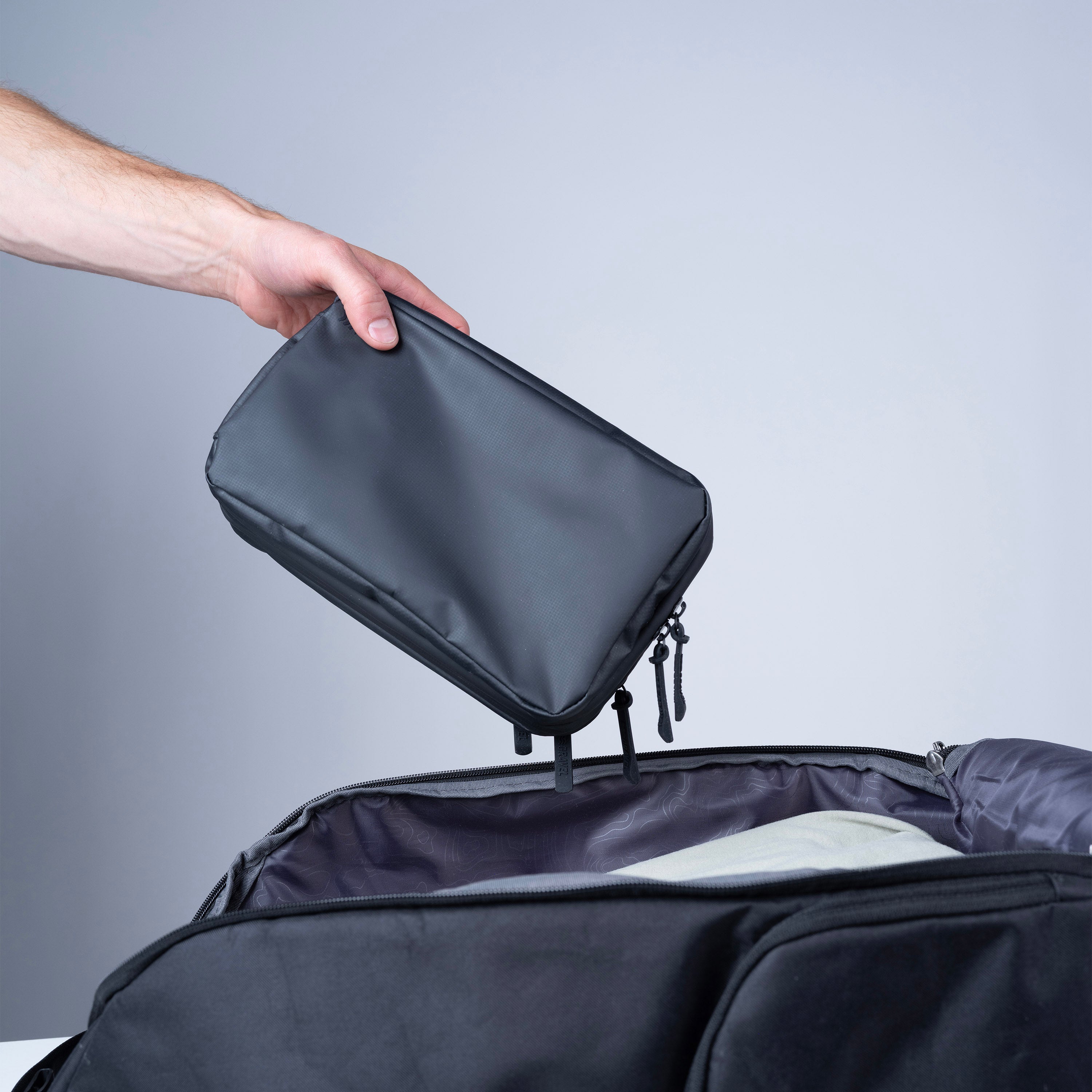Hand opening a black travel bag with a gray background