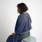 Person wearing a blue quilted jacket sitting on a stool against a white background
