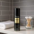 TRESemmé hair spray can on a bathroom shelf with a towel and cotton swabs. It is in a 1.5 oz, TSA-friendly container.