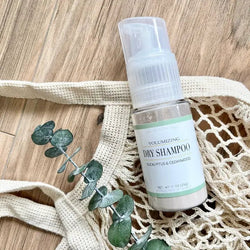 Dry shampoo bottle on a wooden table with a mesh bag and eucalyptus