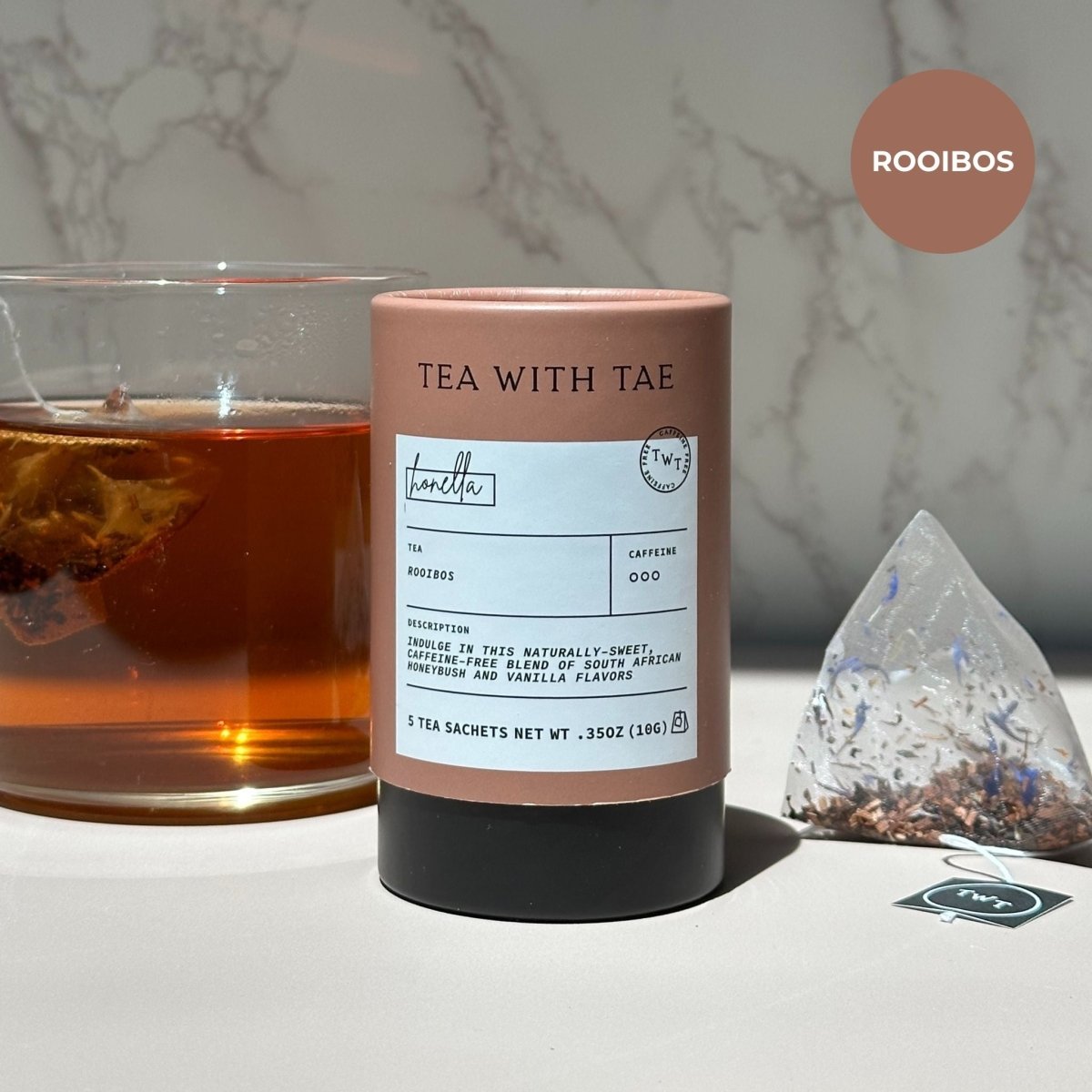 Tea canister labeled 'Tea with Tae' next to a glass of tea on a marble surface