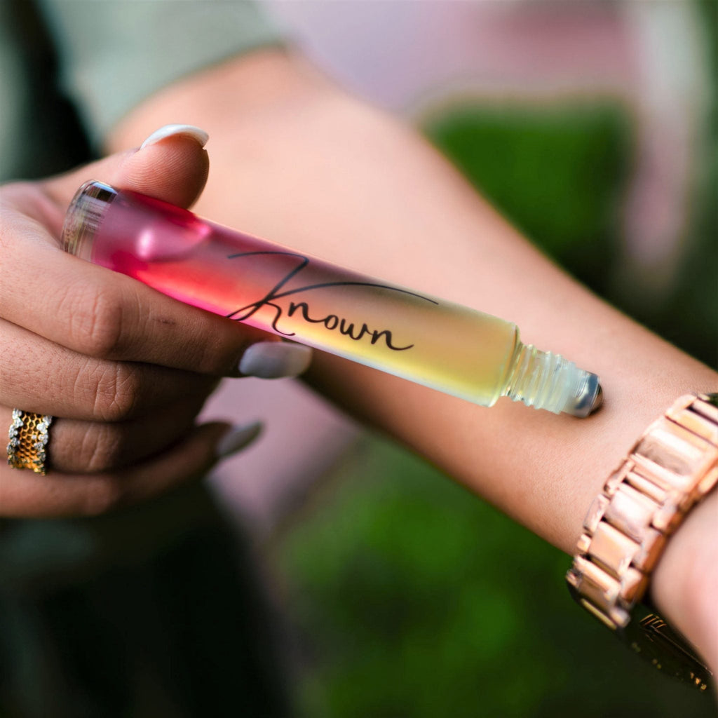 Roll-on bottle of perfume with a gradient design held by a person outdoors.