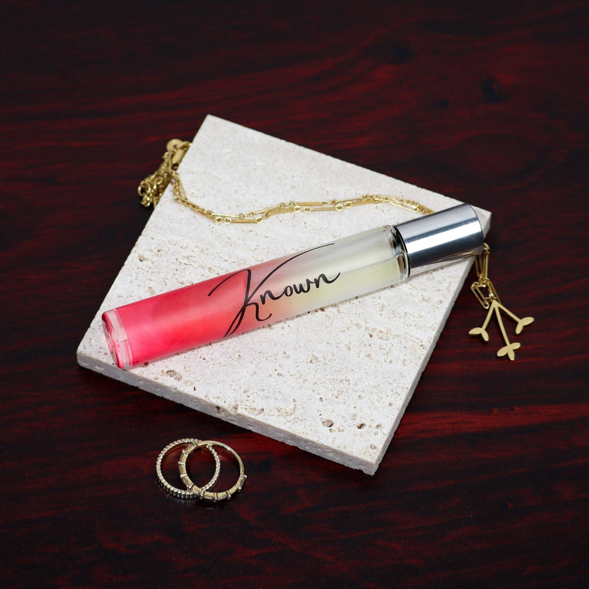 Perfume bottle with gradient design on a stone surface, surrounded by jewelry on a dark wooden background