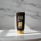 A 3 fl oz travel tube of L'Oréal Paris Elvive Total Repair 5 Repairing Conditioner on a white marble surface with soft sunlight shadows