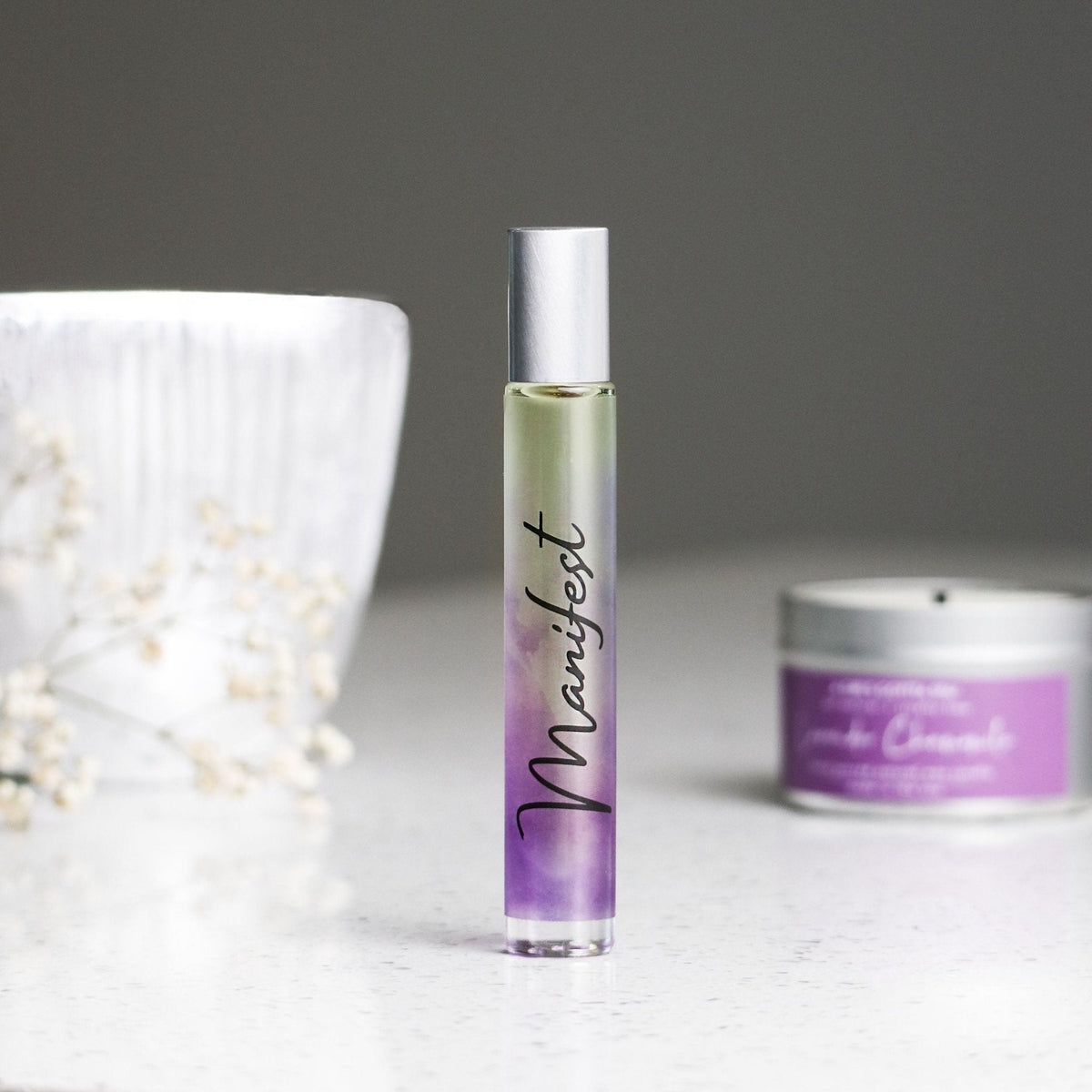 Roll-on bottle labeled 'Manifest' with a purple gradient design on a gray background.
