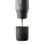 Portable coffee maker dispensing coffee into a black cup on a white background