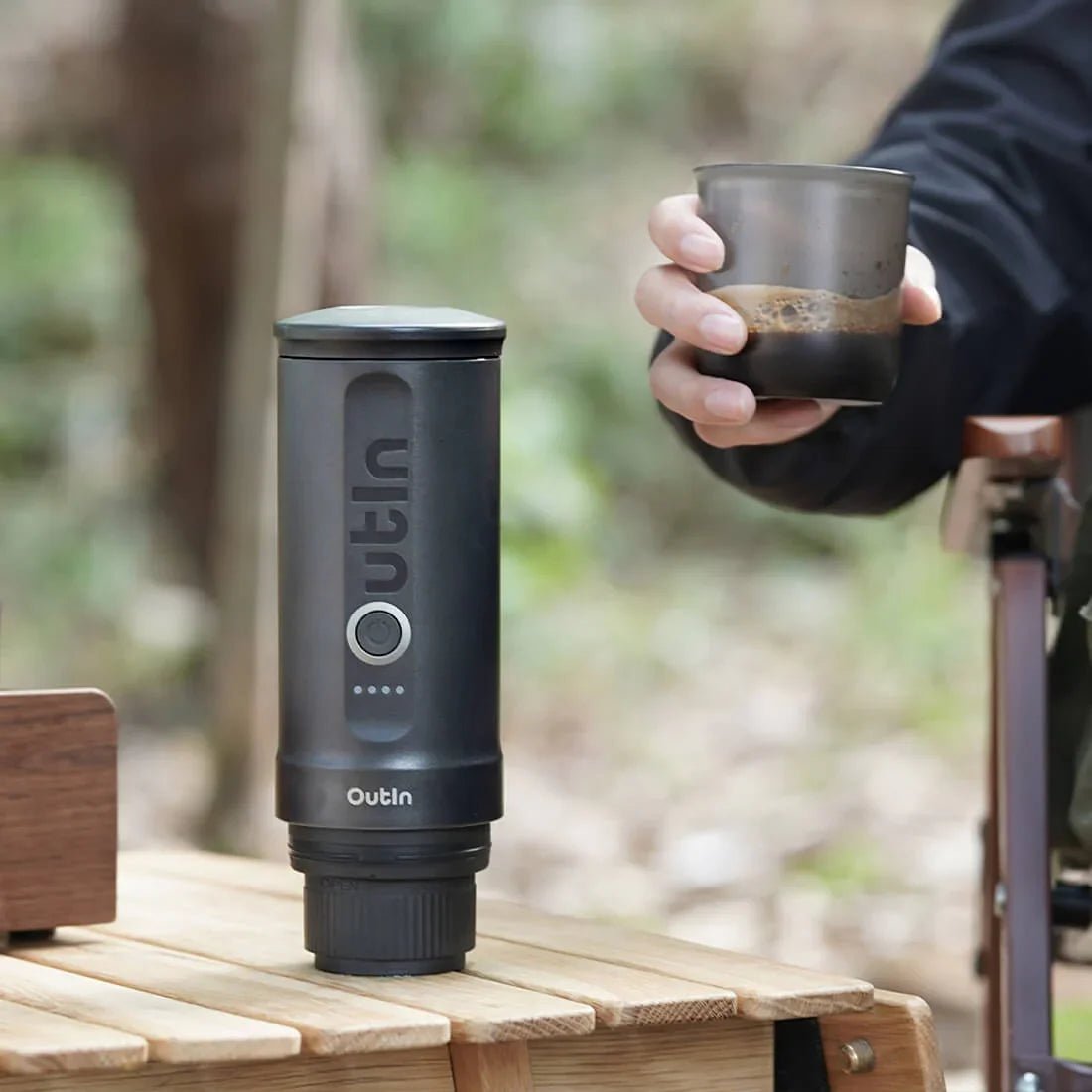 Black portable coffee maker on a wooden surface with a blurred natural background