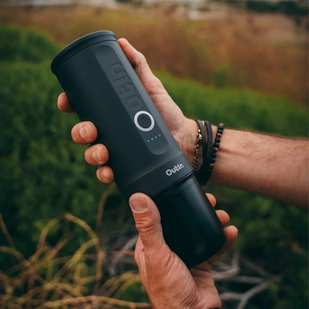 Person holding a black OXO coffee grinder outdoors