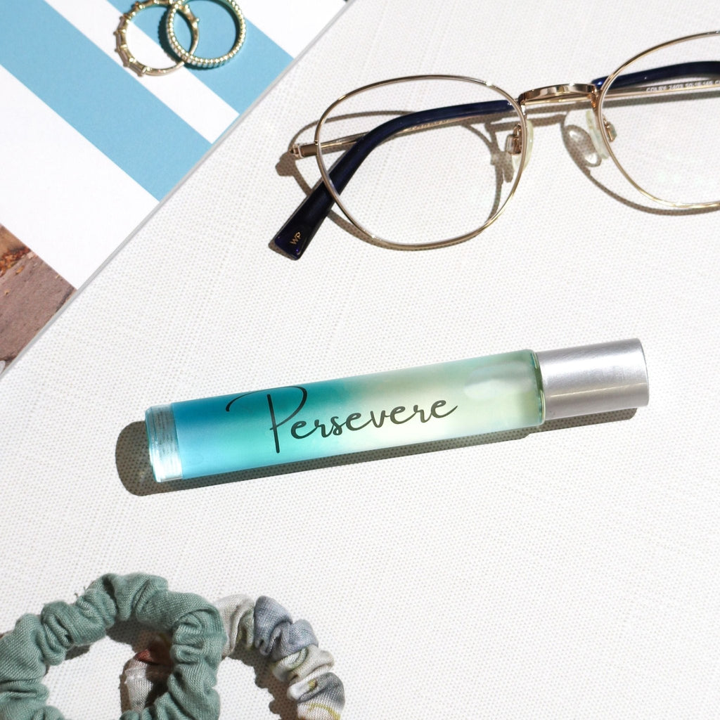 Roll-on bottle with 'Persevere' text, glasses, and scrunchies on a textured surface