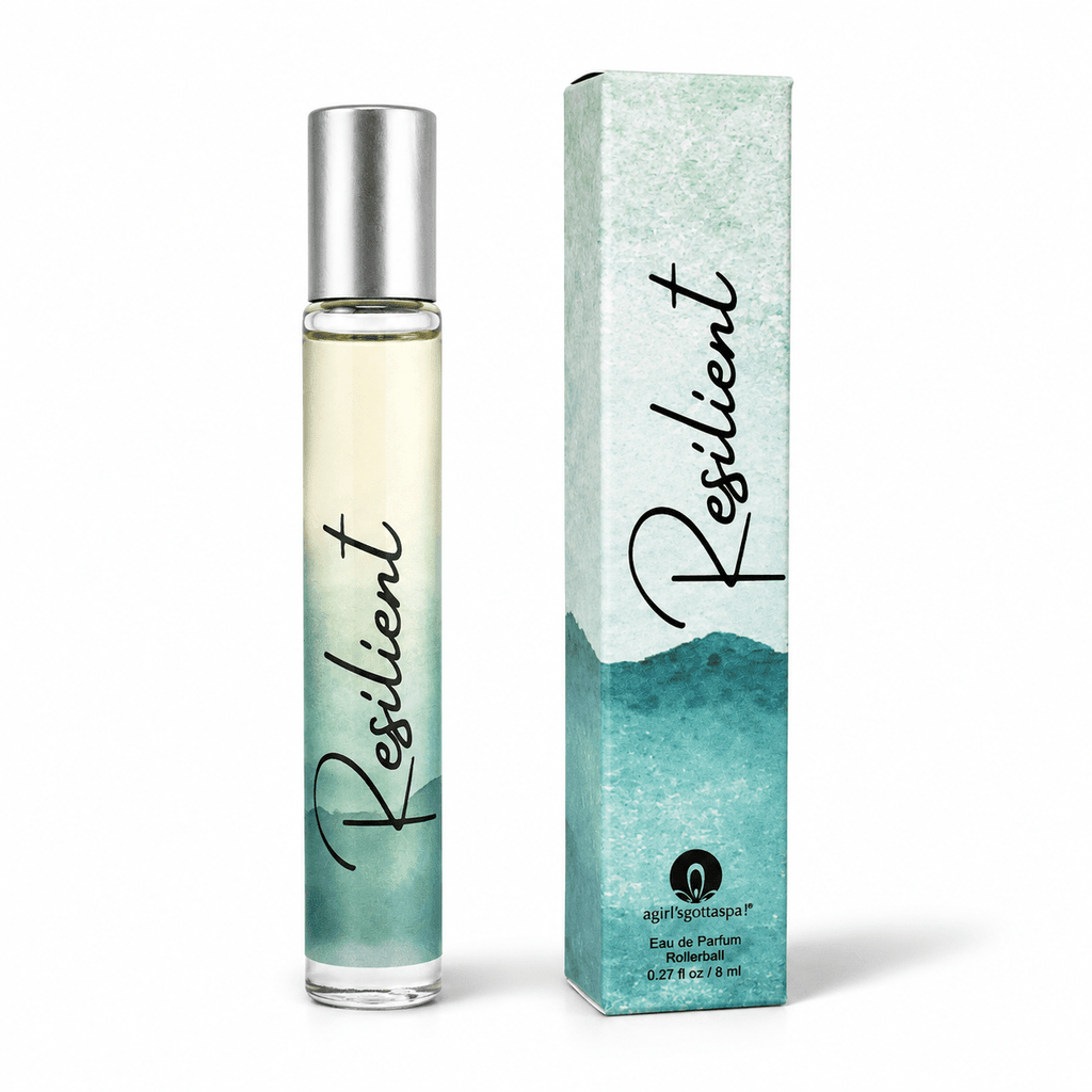 A clear cylindrical perfume bottle with a silver cap stands next to its matching rectangular box. Both the bottle and box feature a teal and aqua watercolor design with the word 'Resilient' in black script.