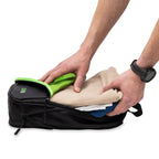 Person packing clothes into a black travel bag with green accents on a white background