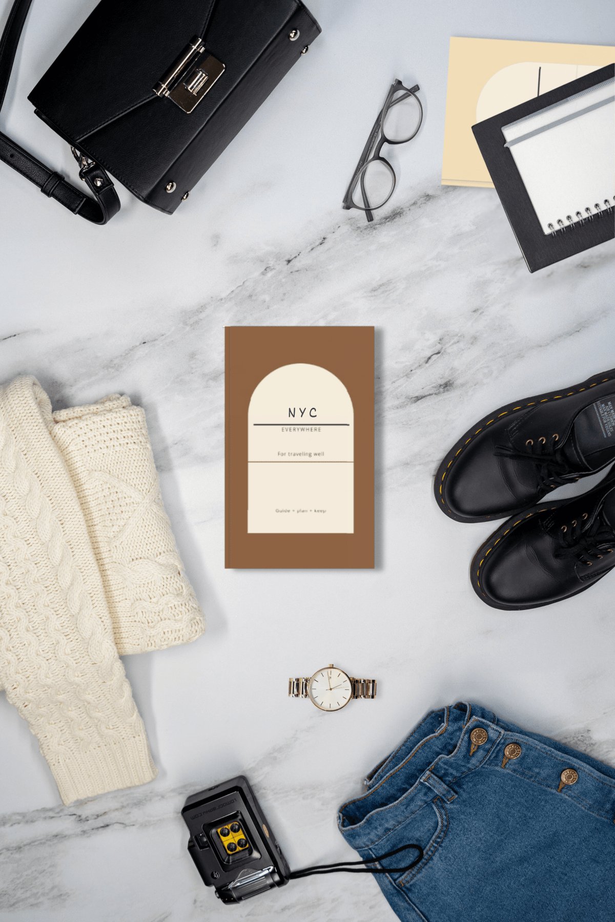 Brown Everywhere travel planner journal in a flat lay with a bag, sweater, boots and sunglasses