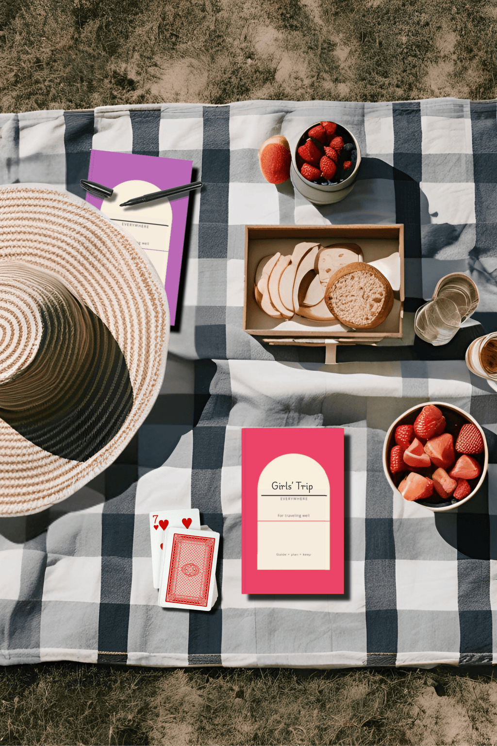 Pink and purple Everywhere travel planners on a picnic blanket with a sun hat and snacks