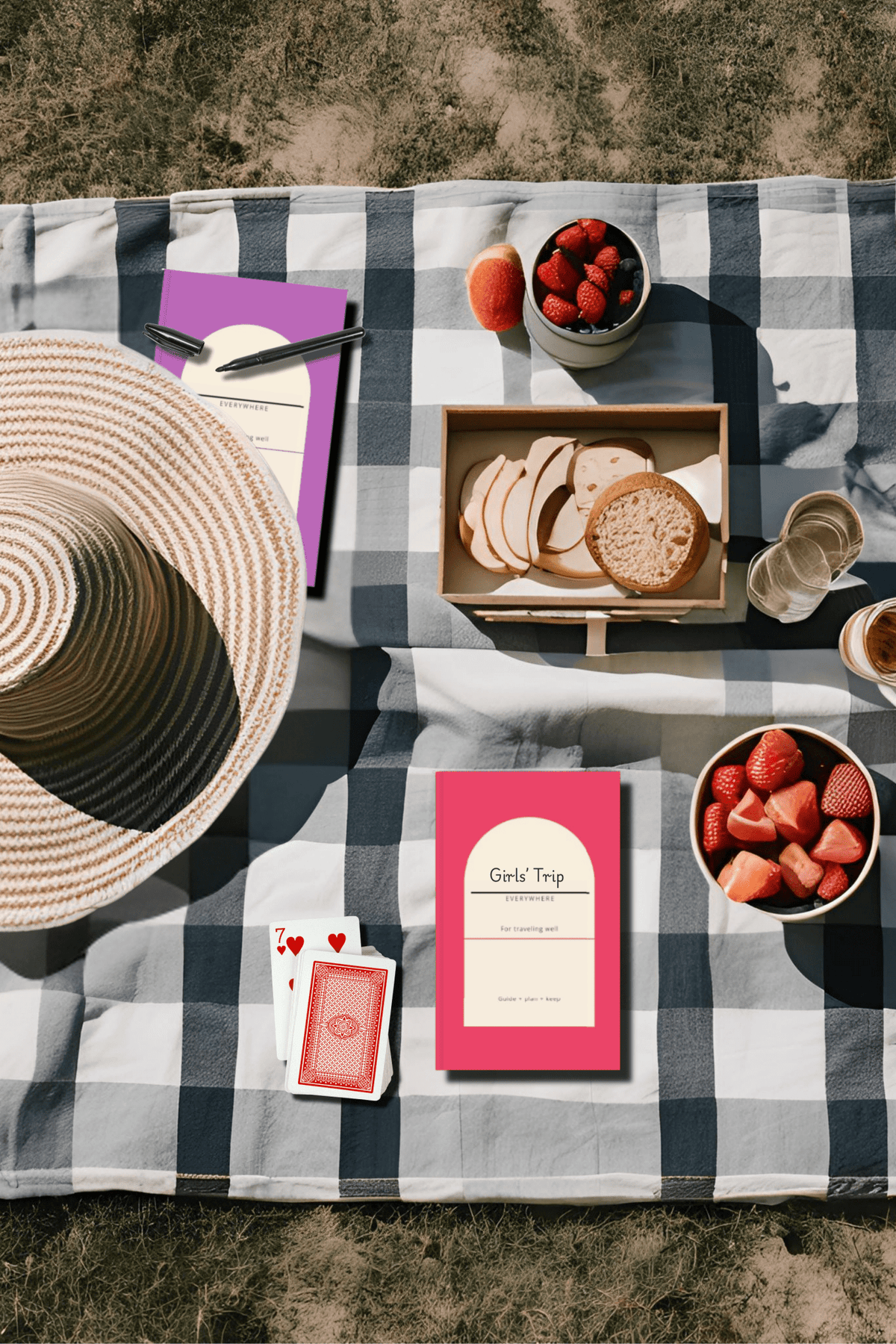 Pink and purple Everywhere travel planners on a picnic blanket with a sun hat and snacks